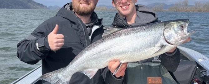 Two men on a boat holding a large salmon